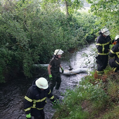 Feuerwehrleute waten durch den Bach, in dem sie mit einem Feuerwehrschlauch eine Sperre errichtet haben.