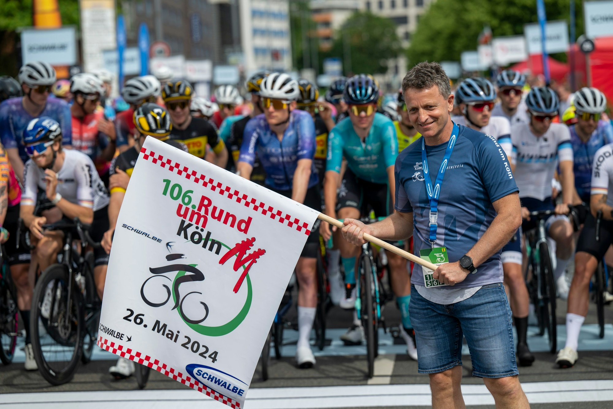 Ein Mann hält eine Flagge, hinter ihm warten Rennradfahrer.
