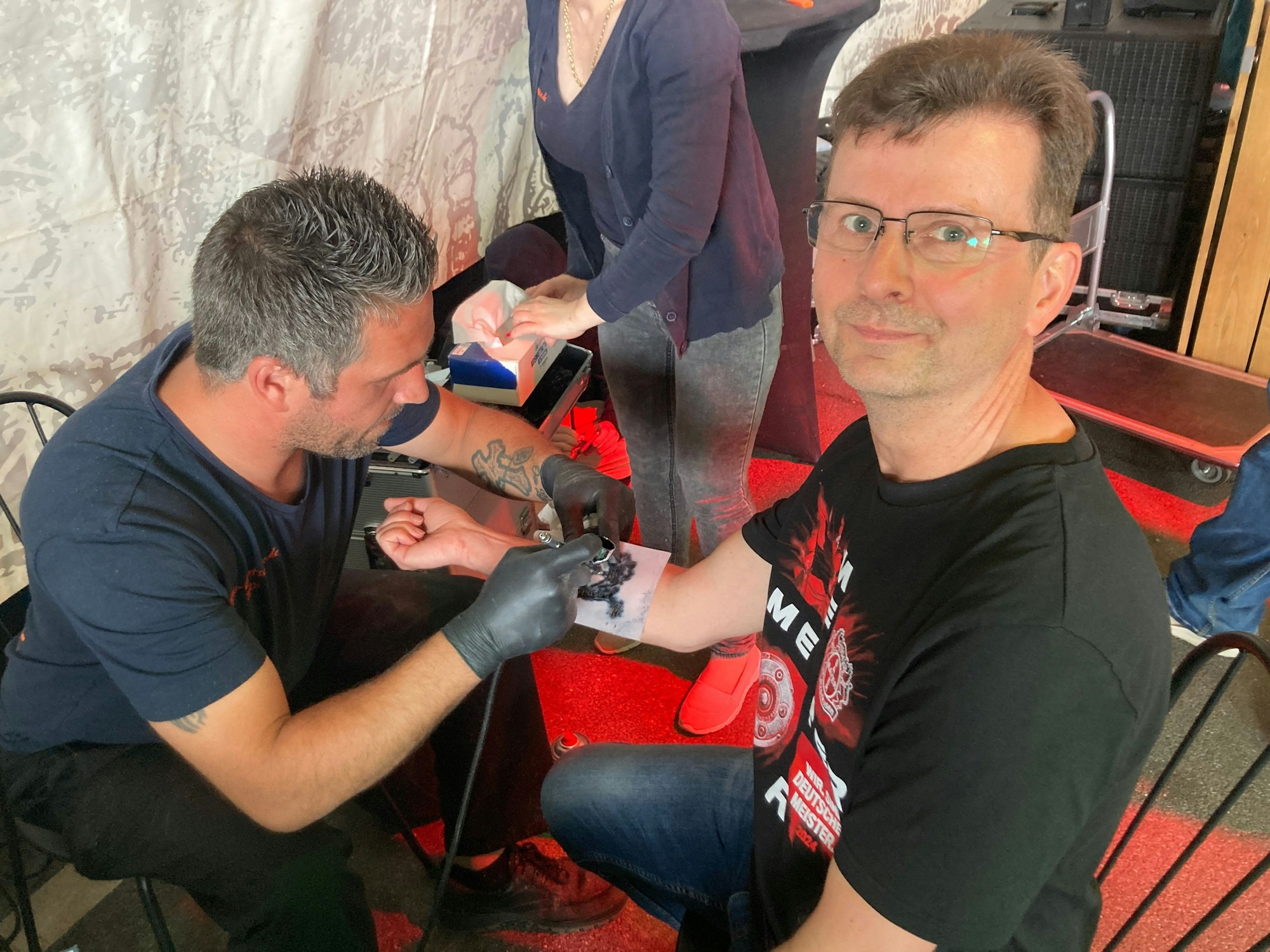Frank Engels möchte den besonderen Moment mit einem Kunstwerk festhalten. Er lässt sich das Bayer-Logo auf den Unterarm tätowieren. Der Moment ist zwar für die Ewigkeit, das Tattoo vorerst jedoch nicht. Es handelt sich um ein Airbrush-Tattoo. „Beim nächsten Double wird es dann ein echtes“, scherzt der Tätowierer.