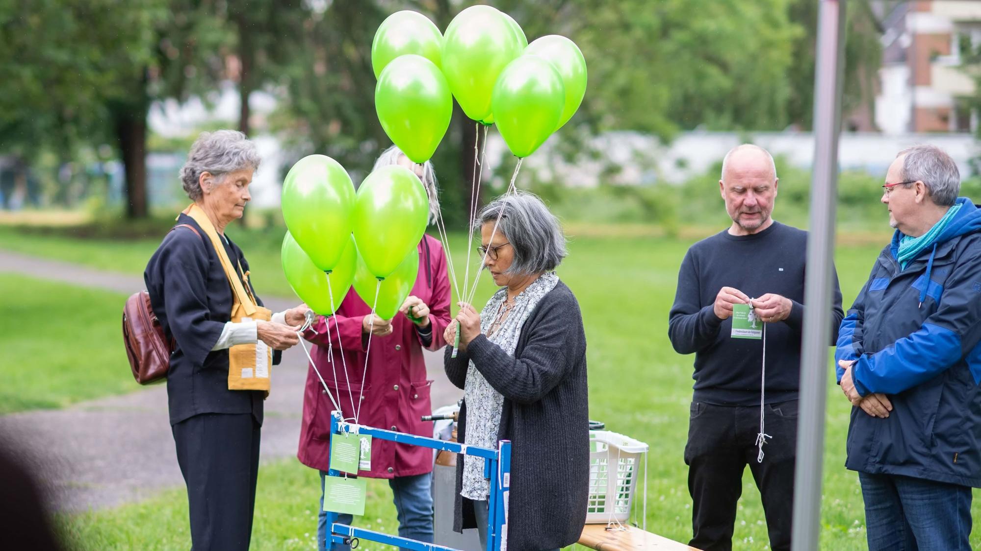 Drei Frauen befestigen Zettel mit Botschaften an den grünen Ballons.