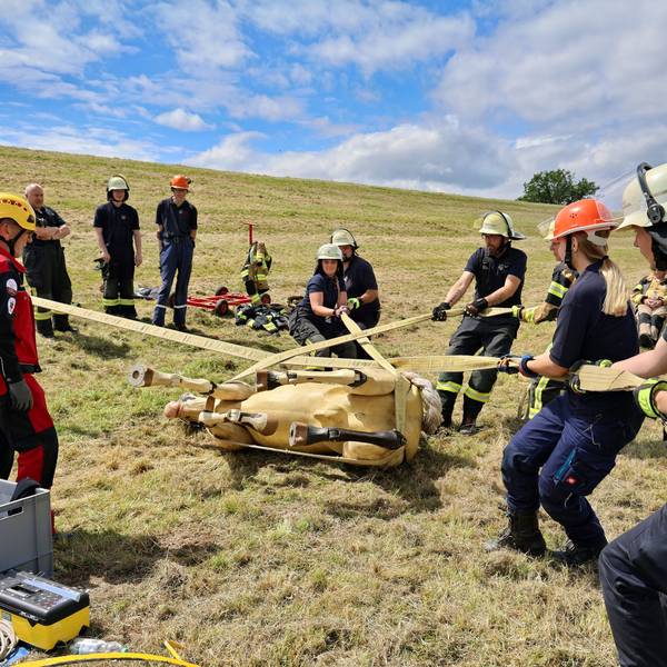 Mithilfe von Bändern drehen acht Feuerwehrleute den liegenden Pferdedummy langsam und kontrolliert auf die andere Seite. Trainer Lutz Hauch gibt Anweisungen.