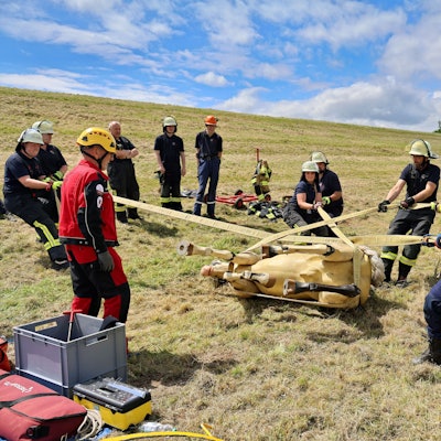 Mithilfe von Bändern drehen acht Feuerwehrleute den liegenden Pferdedummy langsam und kontrolliert auf die andere Seite. Trainer Lutz Hauch gibt Anweisungen.