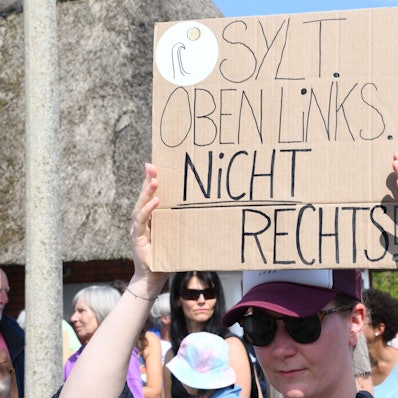 „Sylt oben links. Nicht rechts!“· steht auf einem Plakat, das eine Frau bei einer Mahnwache am Sonntag auf Sylt in der Hand hält. Im Strönwai in Kampen, wo sich auch der Pony-Club befindet, versammelten sich am 26. Mai rund 80 Menschen anlässlich des Rassismus-Eklats um ein Partyvideo auf Sylt zu einer Demo.