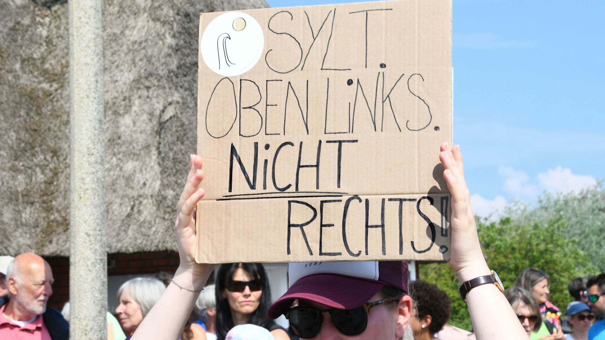 „Sylt oben links. Nicht rechts!“· steht auf einem Plakat, das eine Frau bei einer Mahnwache am Sonntag auf Sylt in der Hand hält. Im Strönwai in Kampen, wo sich auch der Pony-Club befindet, versammelten sich am 26. Mai rund 80 Menschen anlässlich des Rassismus-Eklats um ein Partyvideo auf Sylt zu einer Demo.