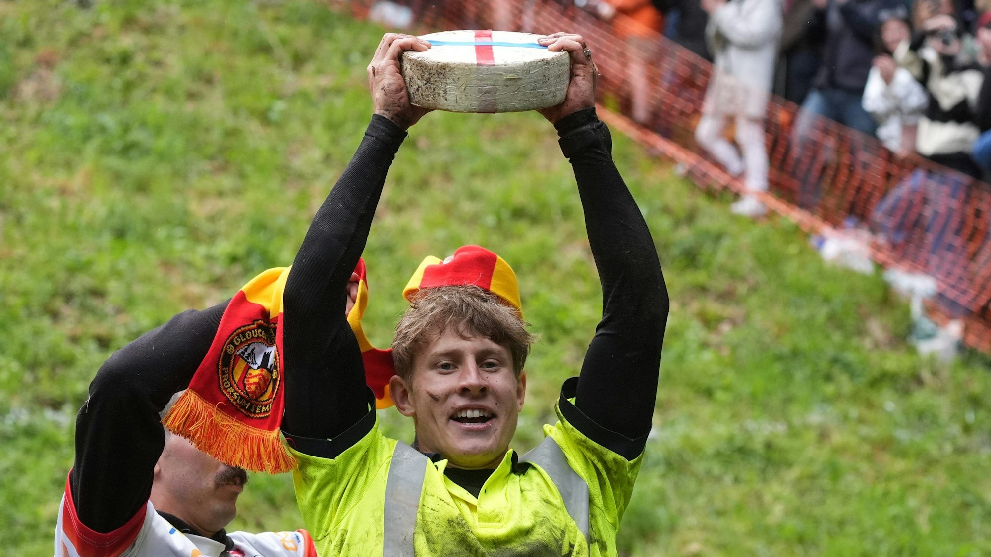 27.05.2024, Großbritannien, Brockworth: Tom Kopke aus Deutschland, der Sieger des ersten Rennens, hebt einen Double-Gloucester-Käse, nachdem er am jährlichen Käserennen "Cheese-Rolling" bei Cooper's Hill teilgenommen hat. Foto: Jacob King/PA Wire/dpa +++ dpa-Bildfunk +++