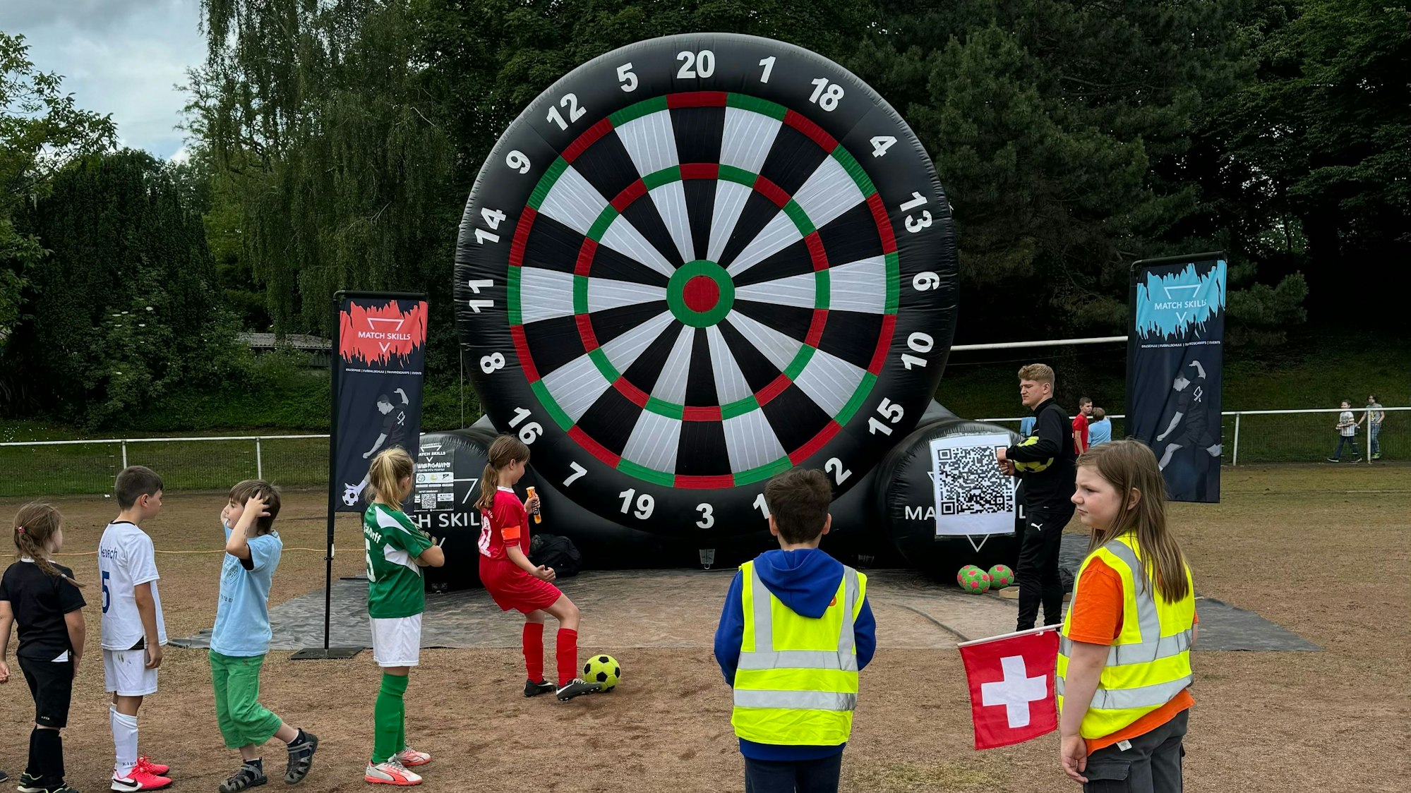 Kinder in Fußballtrikots zielen am Rand des Fußballfeldes auf eine große aufblasbare Zielscheibe.