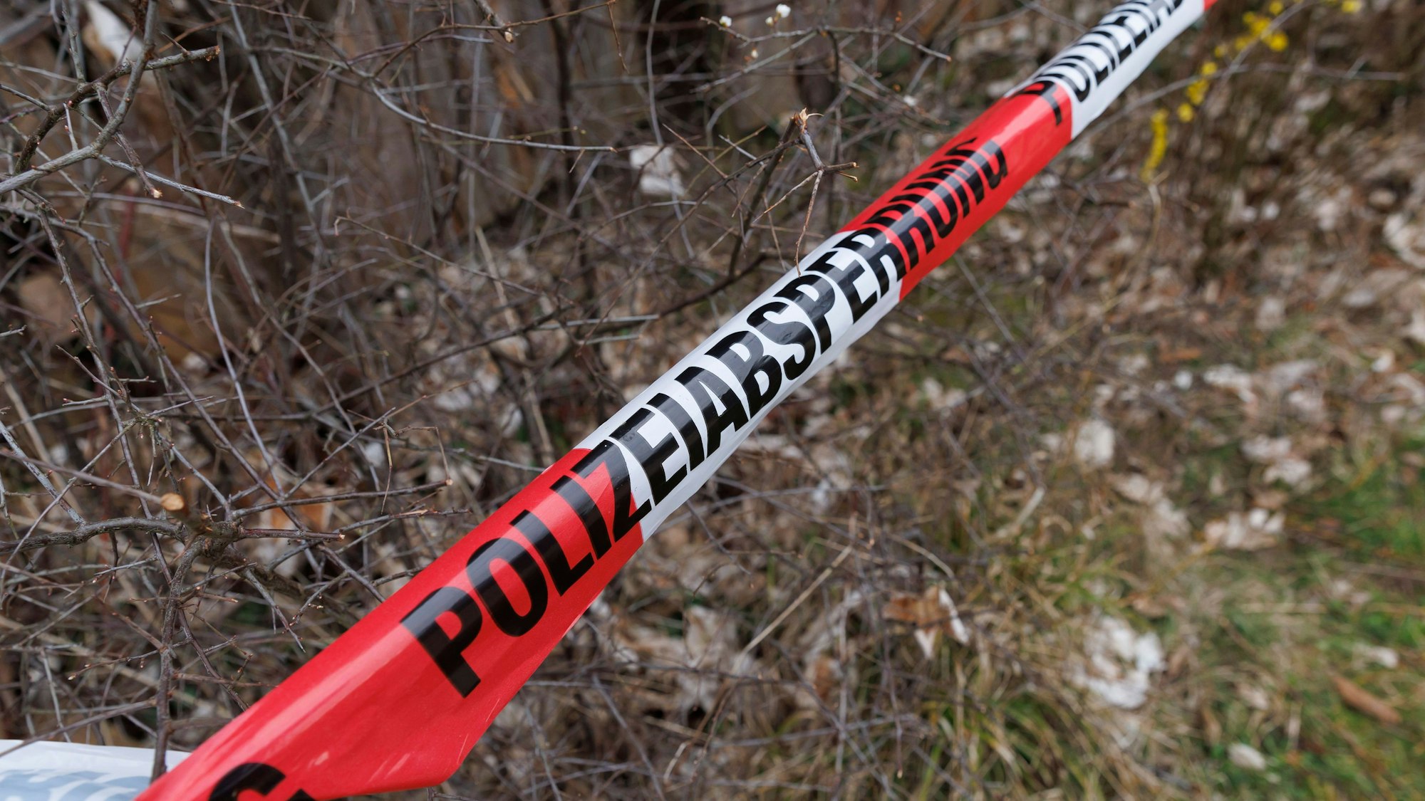 Rot-weißes Flatterband der Polizei ist an einem Tatort zu sehen. Nach dem Fund einer Frauenleiche in einem Waldstück in Ennepetal ist die Identität der mutmaßlich gewaltsam zu Tode gekommenen Frau noch ungeklärt.