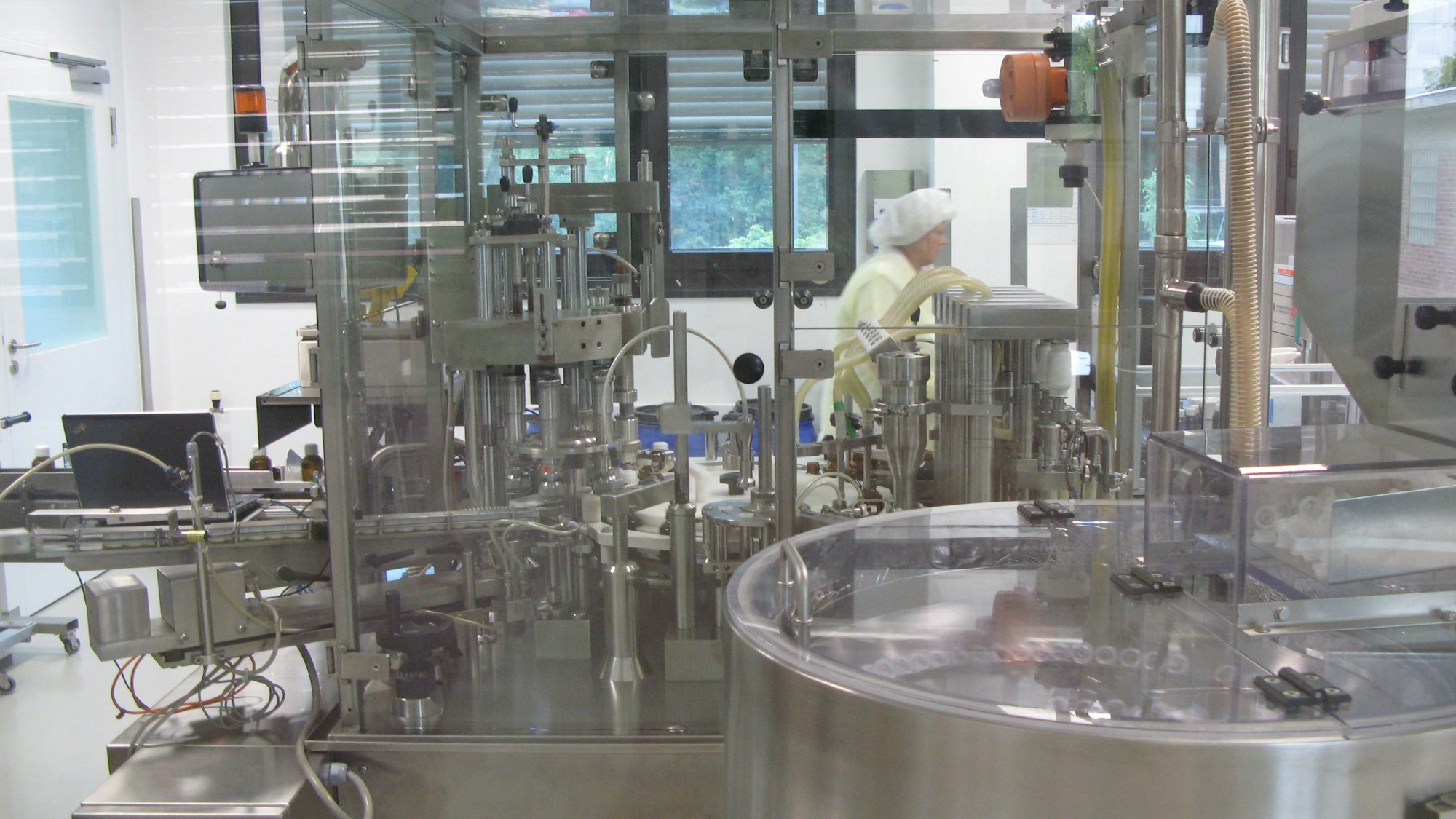 Eine moderne Produktionsstraße mit Stahl und Glas, im Hintergrund eine Person in Kittel und Haube.
