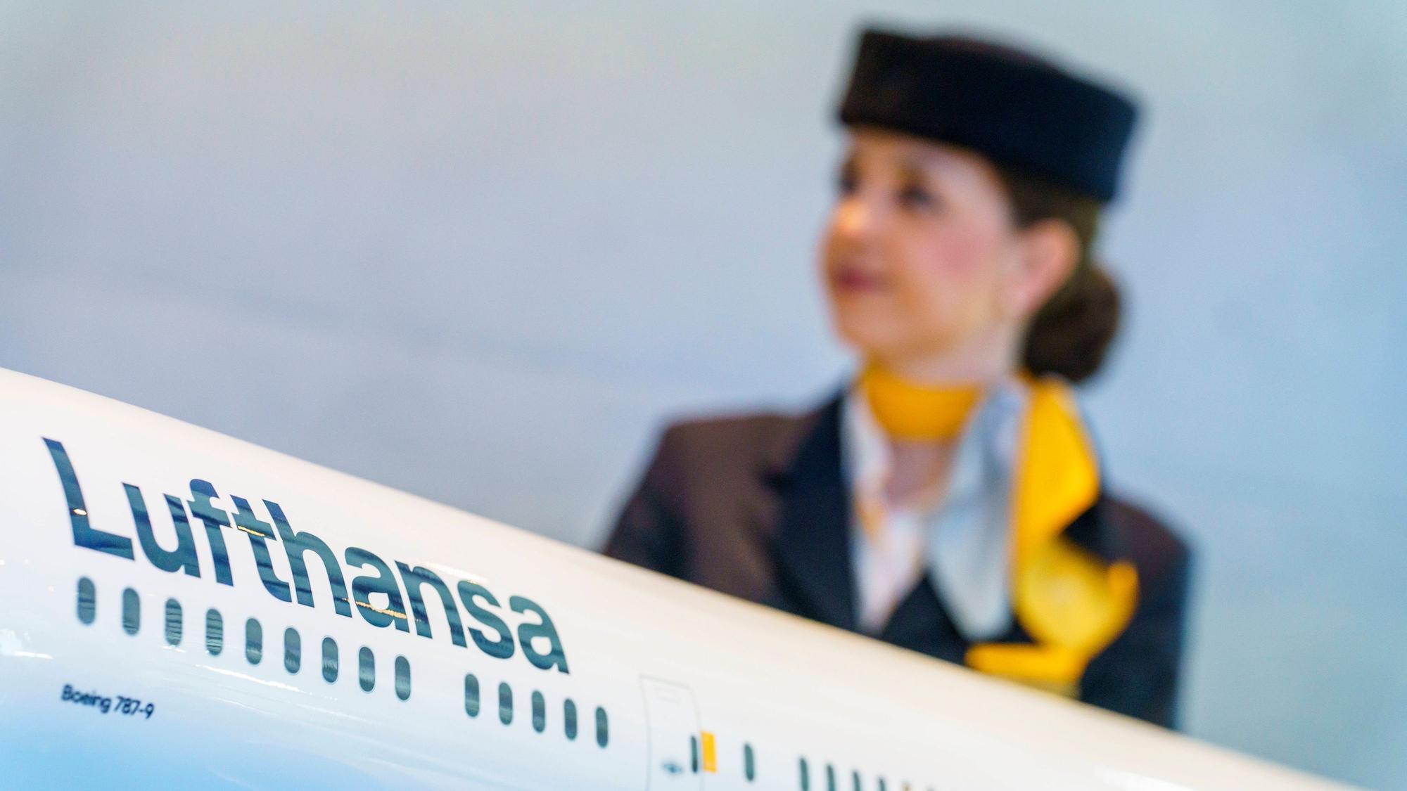 Eine Flugbegleiterin steht hinter einem Modell einer Lufthansamaschine. (Symbolbild)