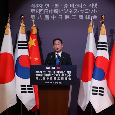 Der japanische Ministerpräsident Fumio Kishida steht an einem Rednerpult vor den Staatsflaggen von Japan, Südkorea und China.