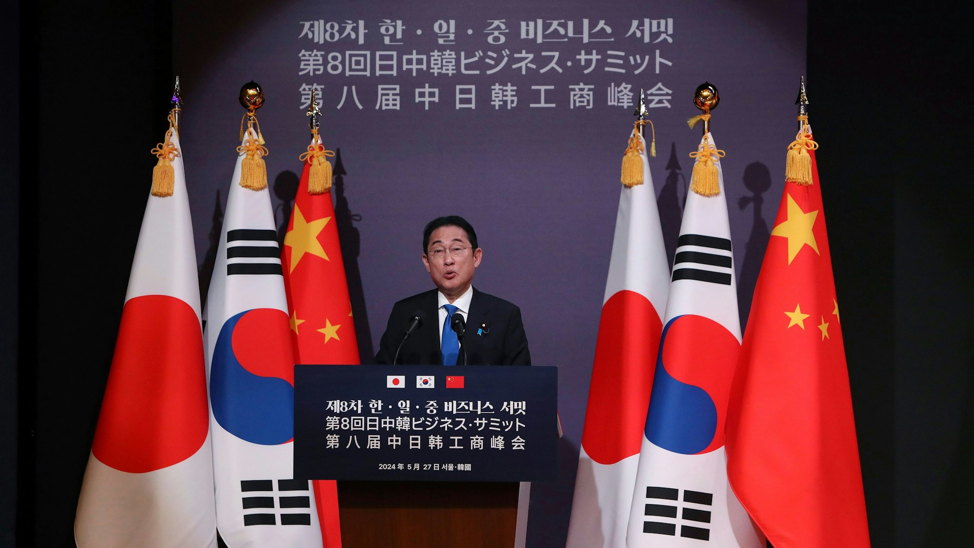 Der japanische Ministerpräsident Fumio Kishida steht an einem Rednerpult vor den Staatsflaggen von Japan, Südkorea und China.