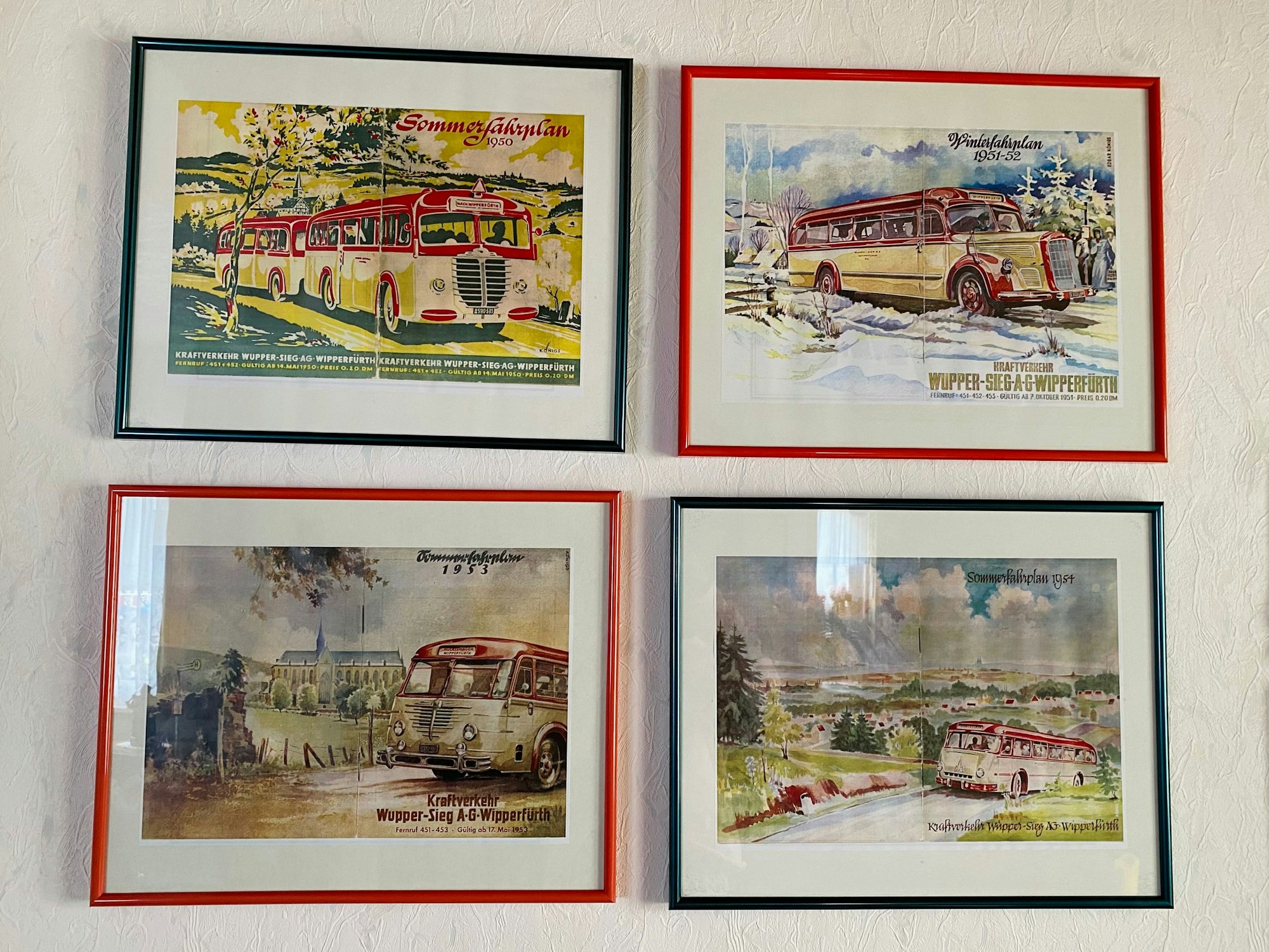 Vier Bilderrahmen mit Zeichnungen von Bussen hängen an einer Wand.