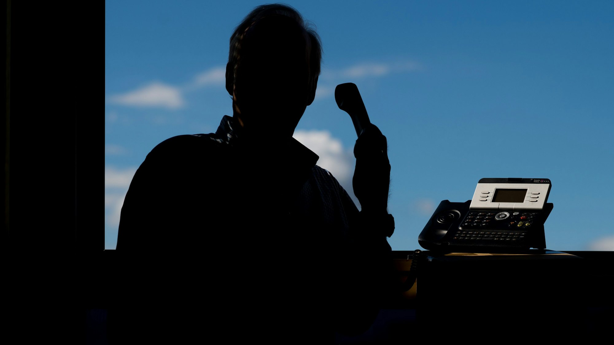 Ein Mann ist nur als Schatten zu erkennen. Er hält ein Telefon in der Hand.