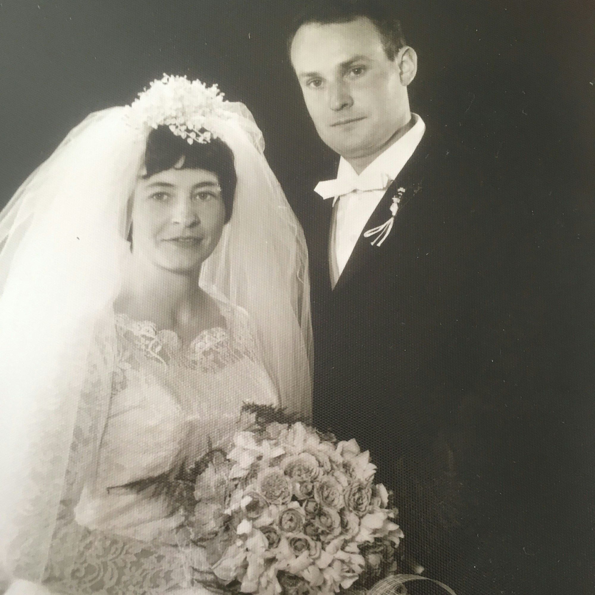 Ein schwarz-weiß Foto eines jungen Brautpaars, sie trägt einen üppigen Schleier und hält einen großen Strauß.