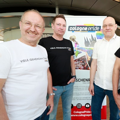Zu sehen sind vier Männer, die vor einem Plakat mit der Aufschrift „cologne pride“ stehen.