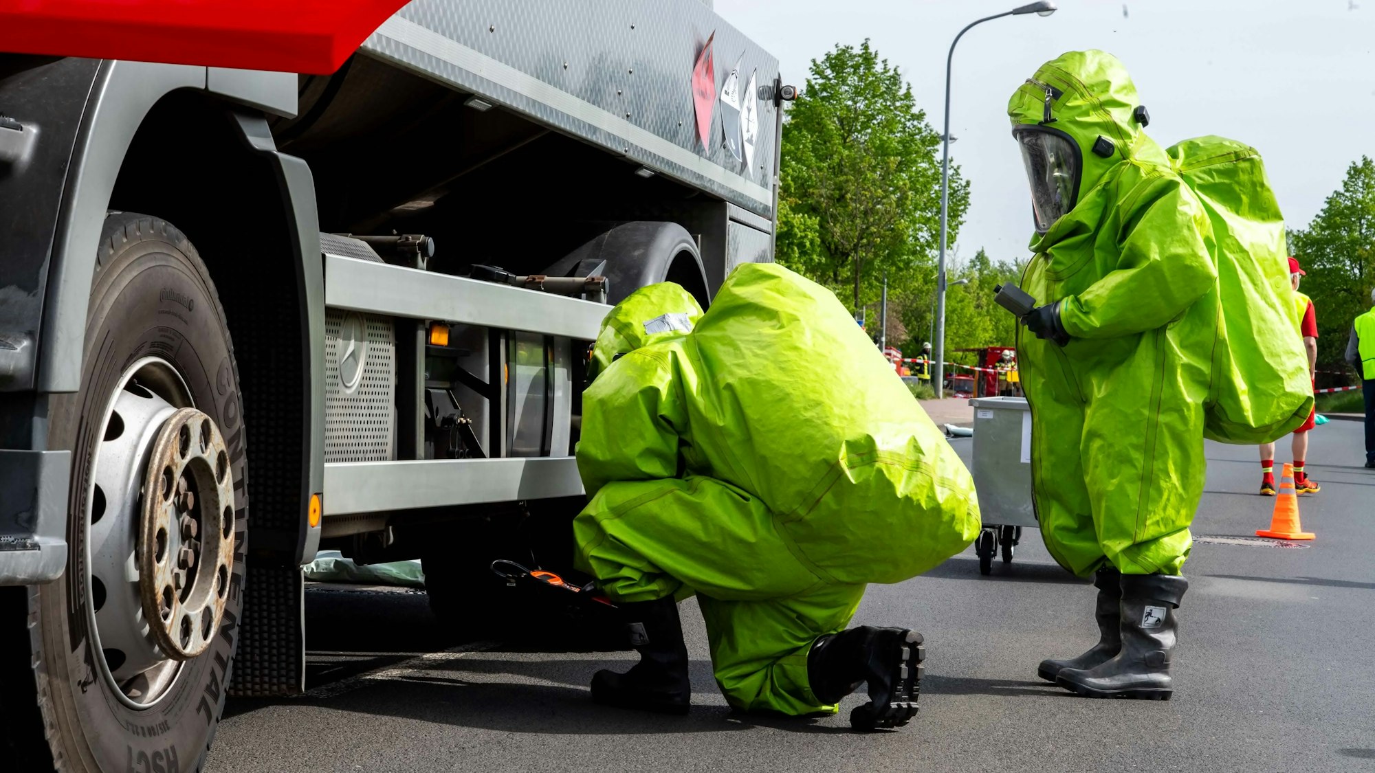 Das Bild zeigt zwei Einsatzkräfte in Schutzanzügen, die an einem Lkw eine Messung durchführen.