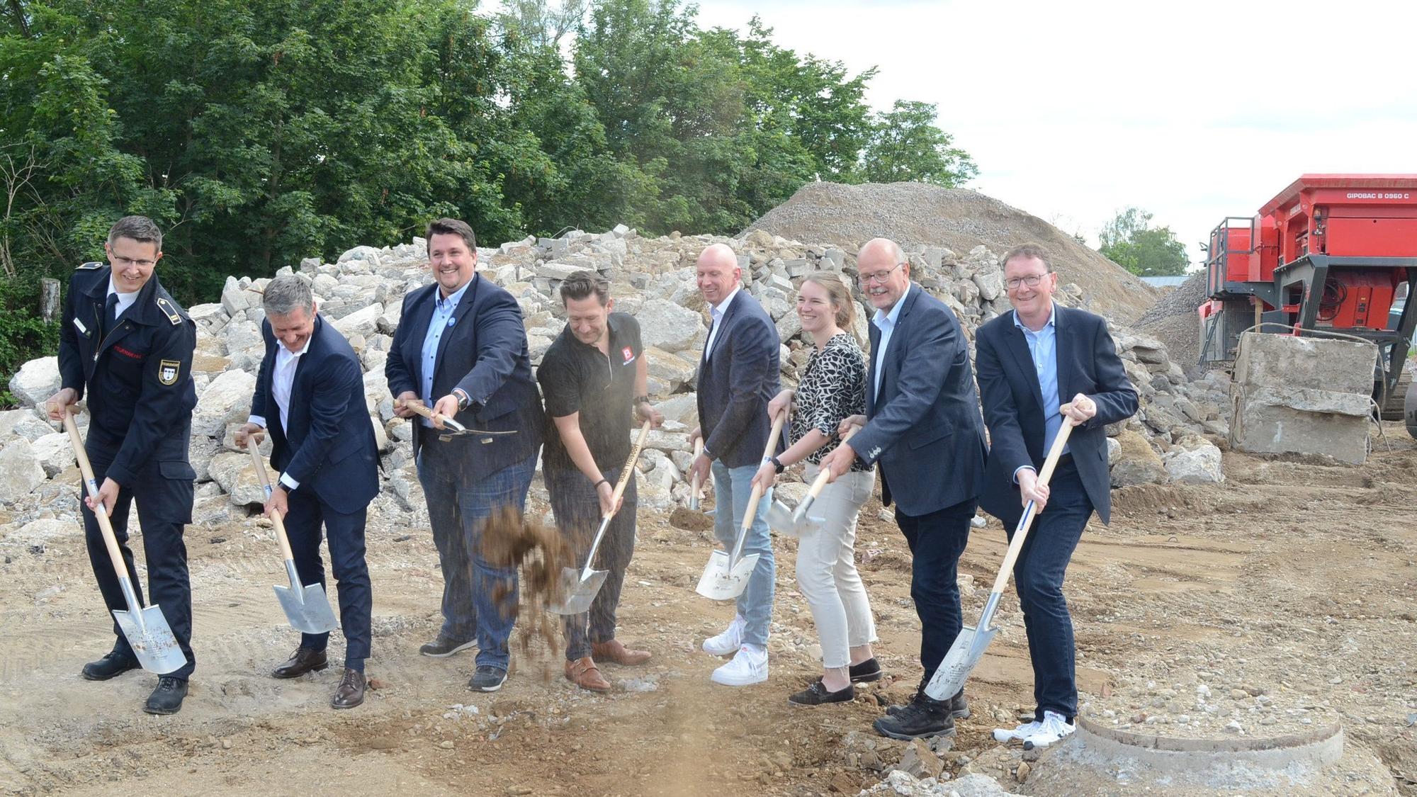 Sieben Männer und eine Frau auf einer Baustelle. Mit Spaten werfen sie Erde in die Luft.