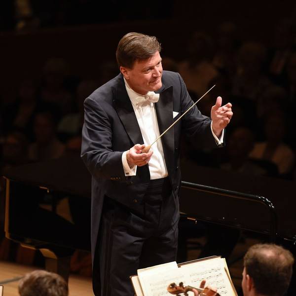 Das Bild zeigt Christian Thielemann, er trägt einen schwarzen Anzug mit weißem Hemd und hält einen Taktstock in der Hand. Er ist seinem Orchester zugewandt.