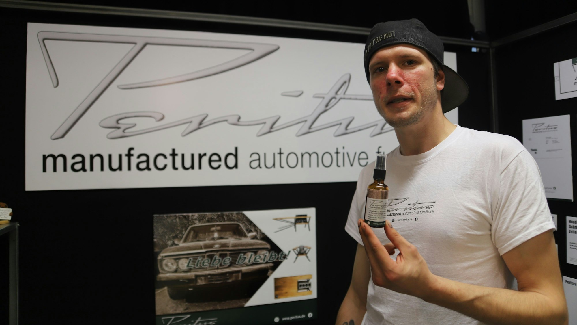 Jan Guhde zeigt ein Lederpflegemittel vor dem Logo seiner Manufaktur.