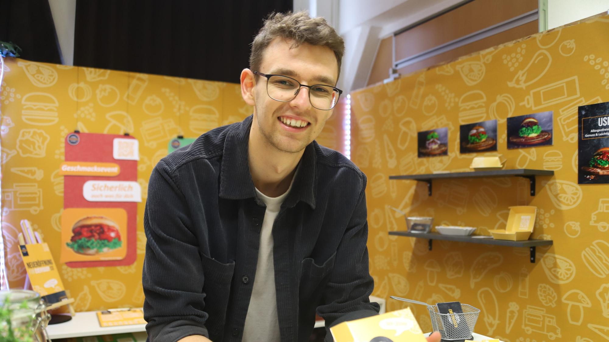 Leon Kunz steht in seinem Stand, der für einen Burger wirbt, der keines der 14 Hauptallergene enthält.