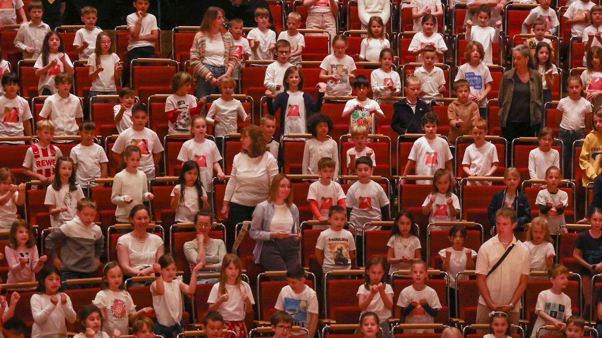 Schülerinnen und Schüler sitzen und stehen beim Singpause-Konzert in den Publikumsreihen der Kölner Philharmonie und singen, klatschen, schunkeln.