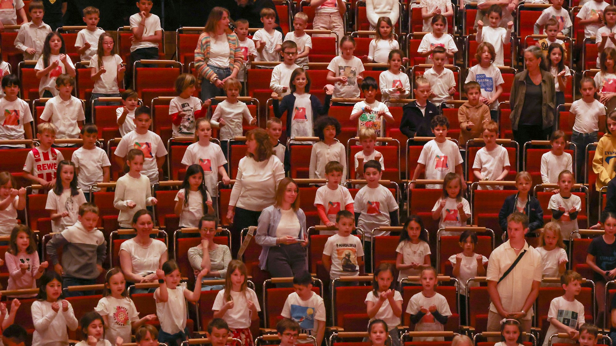 Schülerinnen und Schüler sitzen und stehen beim Singpause-Konzert in den Publikumsreihen der Kölner Philharmonie und singen, klatschen, schunkeln.