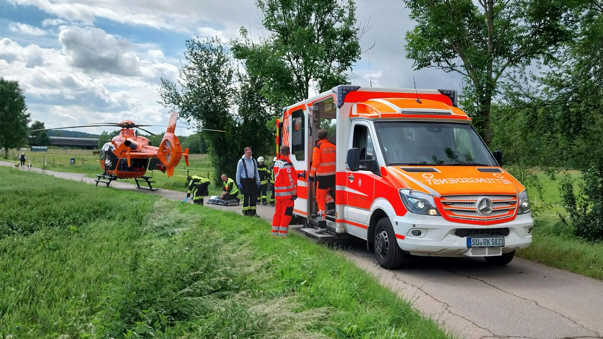 Ein Rettungswagen und der Rettungshubschrauber stehen auf einem schmalen Weg.