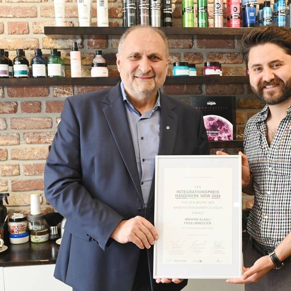 Zwei Männer halten eine Urkunde, während sie in einem Friseursalon stehen.