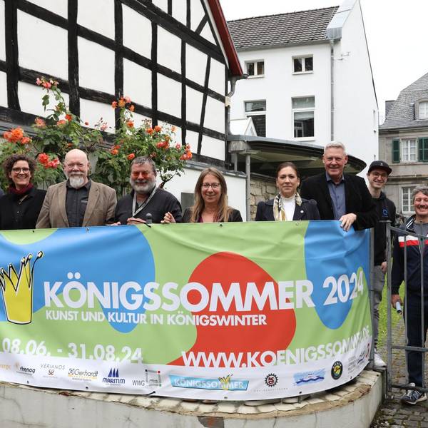 Eine Gruppe von Männern und Frauen stehen hinter einem Transparent mit der Aufschrift „Königssommer 2024“.