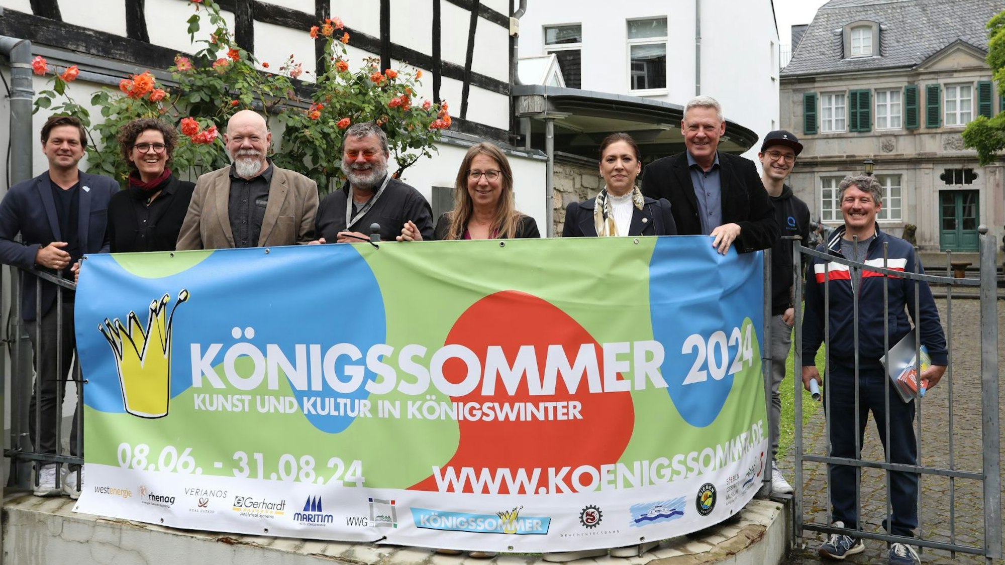 Eine Gruppe von Männern und Frauen stehen hinter einem Transparent mit der Aufschrift „Königssommer 2024“.