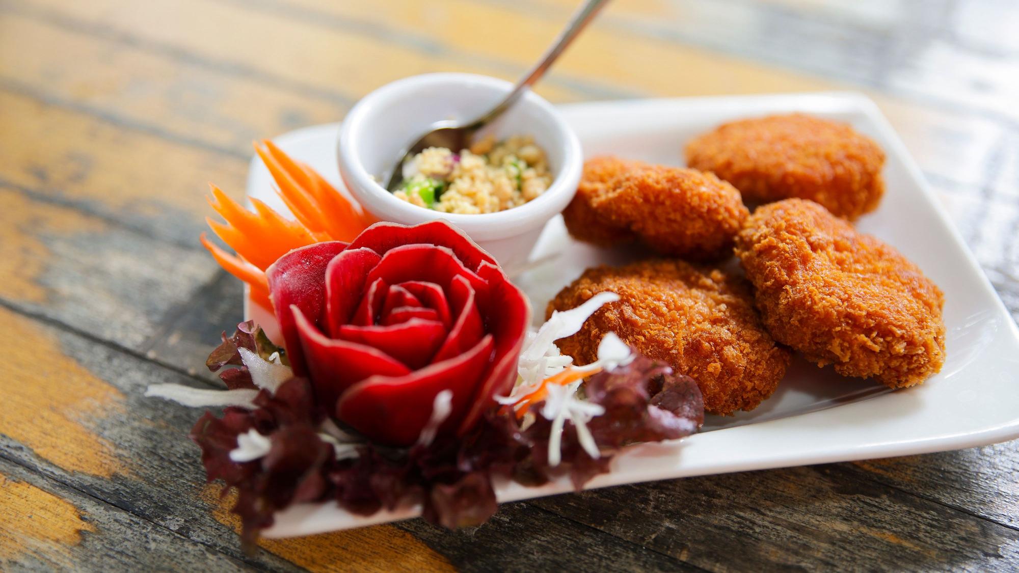 Tordman Guy- Shrimpsfrikadellen liegen auf einem kleinen Teller, daneben dekorative Gemüseschnitzereien und ein Schälchen mit einem Dipp.