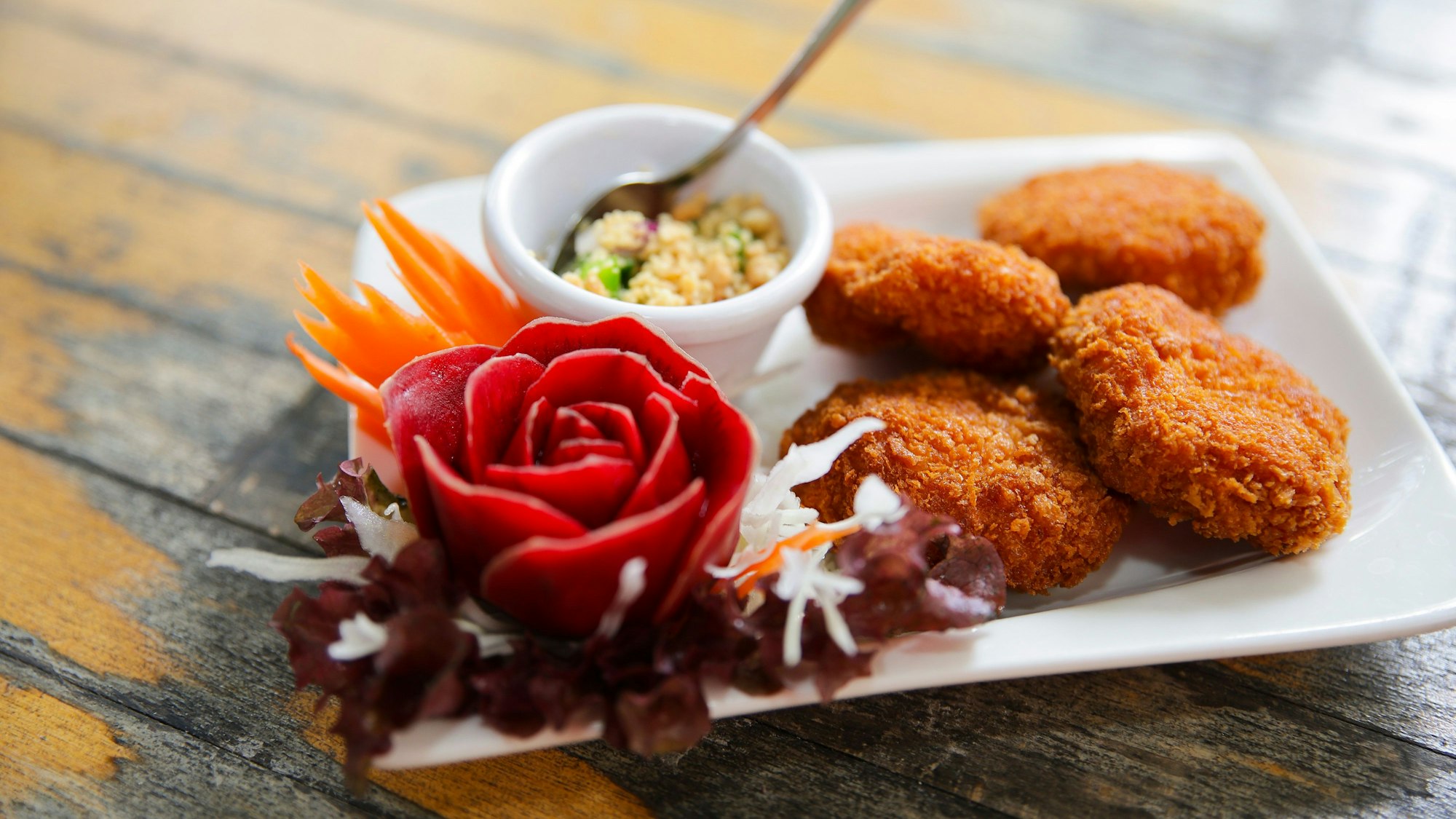 Tordman Guy- Shrimpsfrikadellen liegen auf einem kleinen Teller, daneben dekorative Gemüseschnitzereien und ein Schälchen mit einem Dipp.