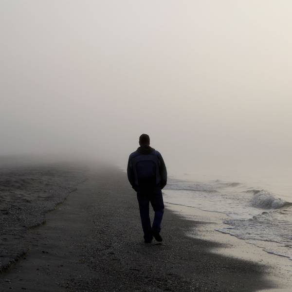 Ein Mann, von dem nur die Umrisse zu erkennen sind, spaziert an einem nebeligen Strand entlang. (Symbolbild)