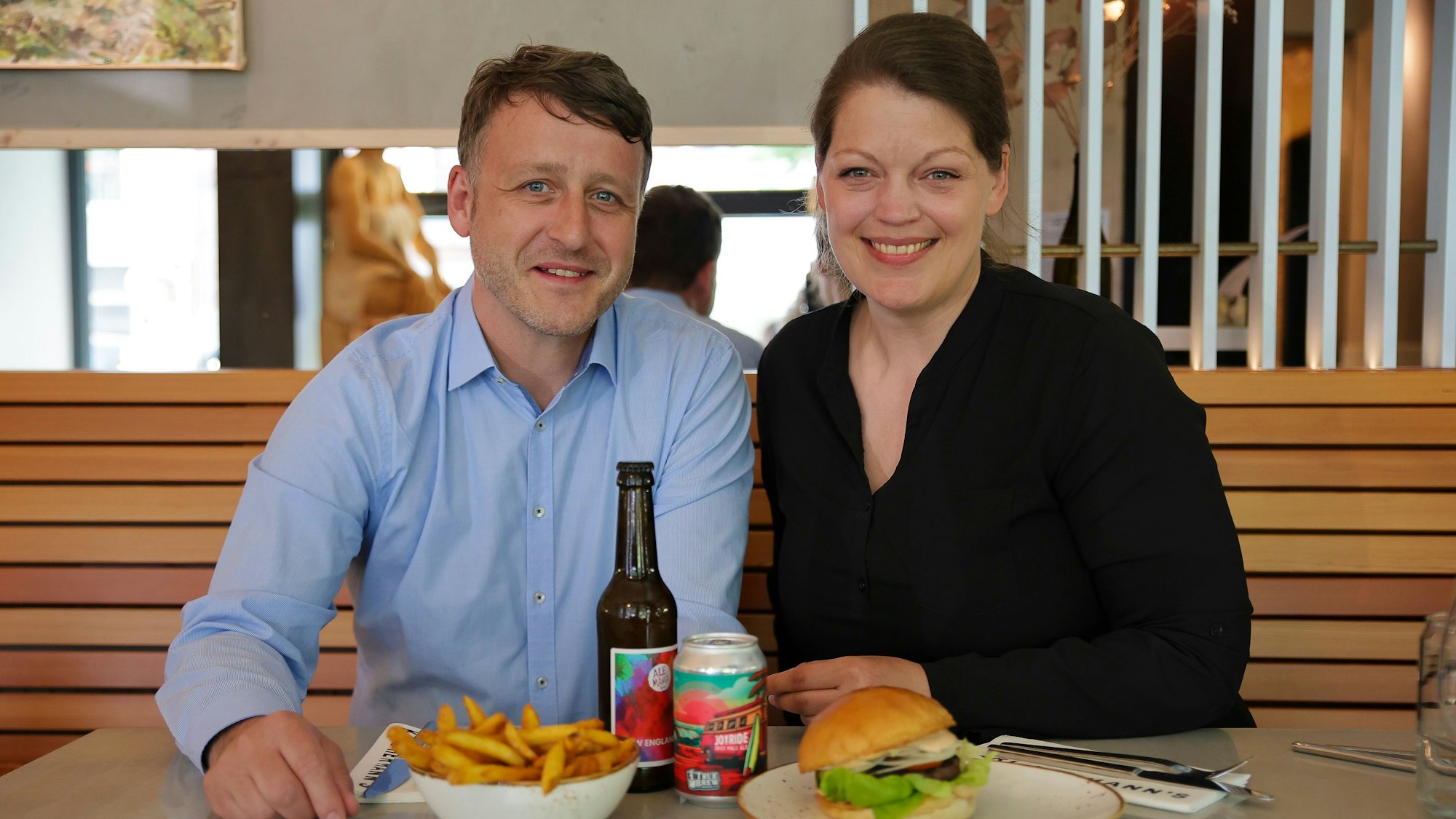 Biersommelière Astrid Berns und Food-Experte Thorsten Lenz sitzen im Burgerladen Herrmanns in Ehrenfeld. Dort gibt es zum Burger das Craftbeer Ale Mania aus Bonn sowie das „True Brew Joyride“ aus München.