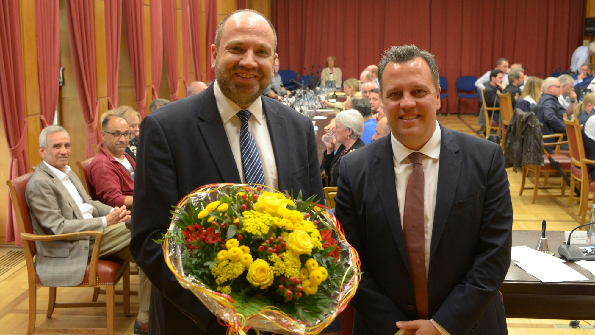 René Strotkötter (l.) und Sacha Reichelt stehen nebeneinander im Ratssaal, hinter ihnen sitzen Stadtverordnete an ihren Tischen.