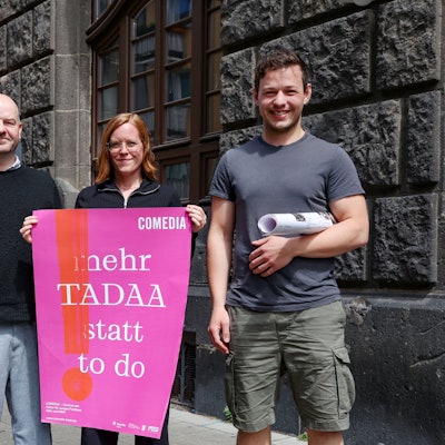 Drei Menschen stehen mit Plakaten vor der Comedia.