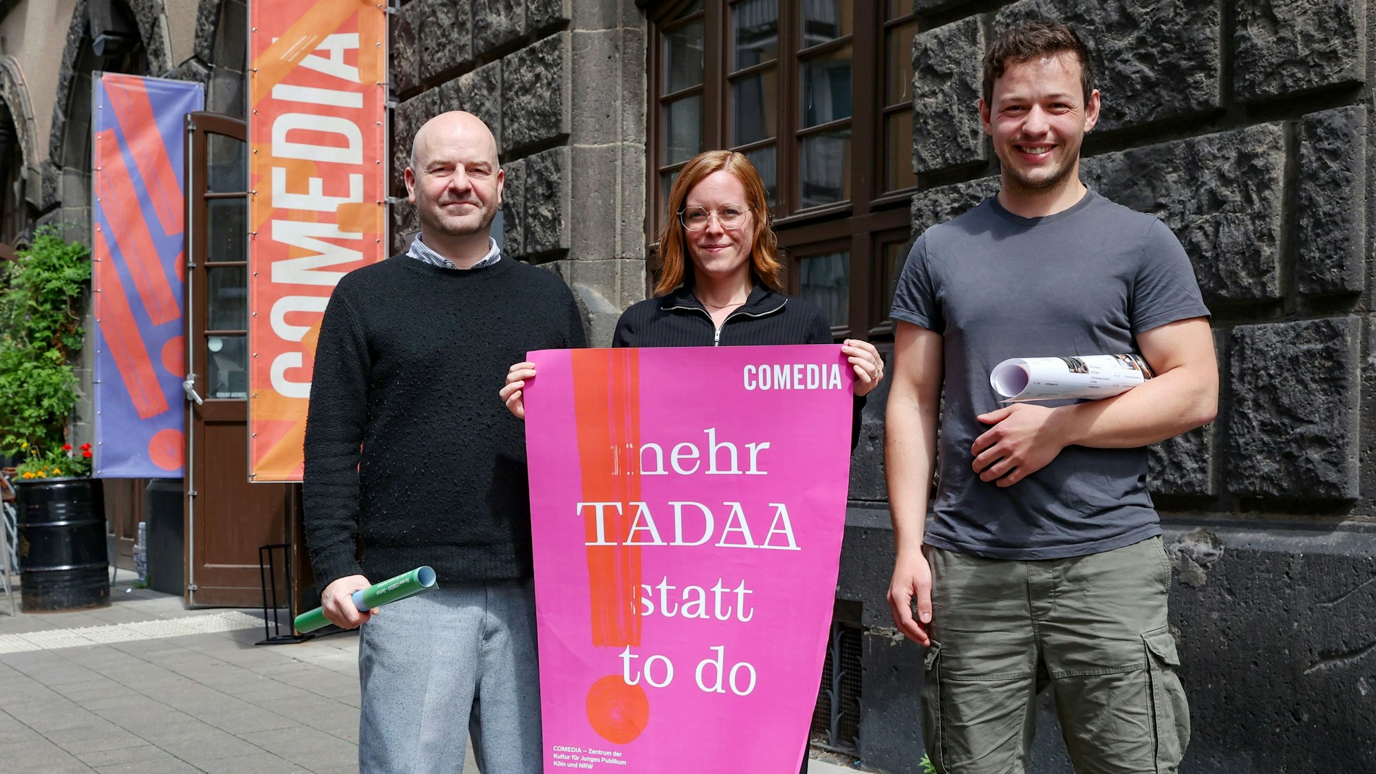Drei Menschen stehen mit Plakaten vor der Comedia.