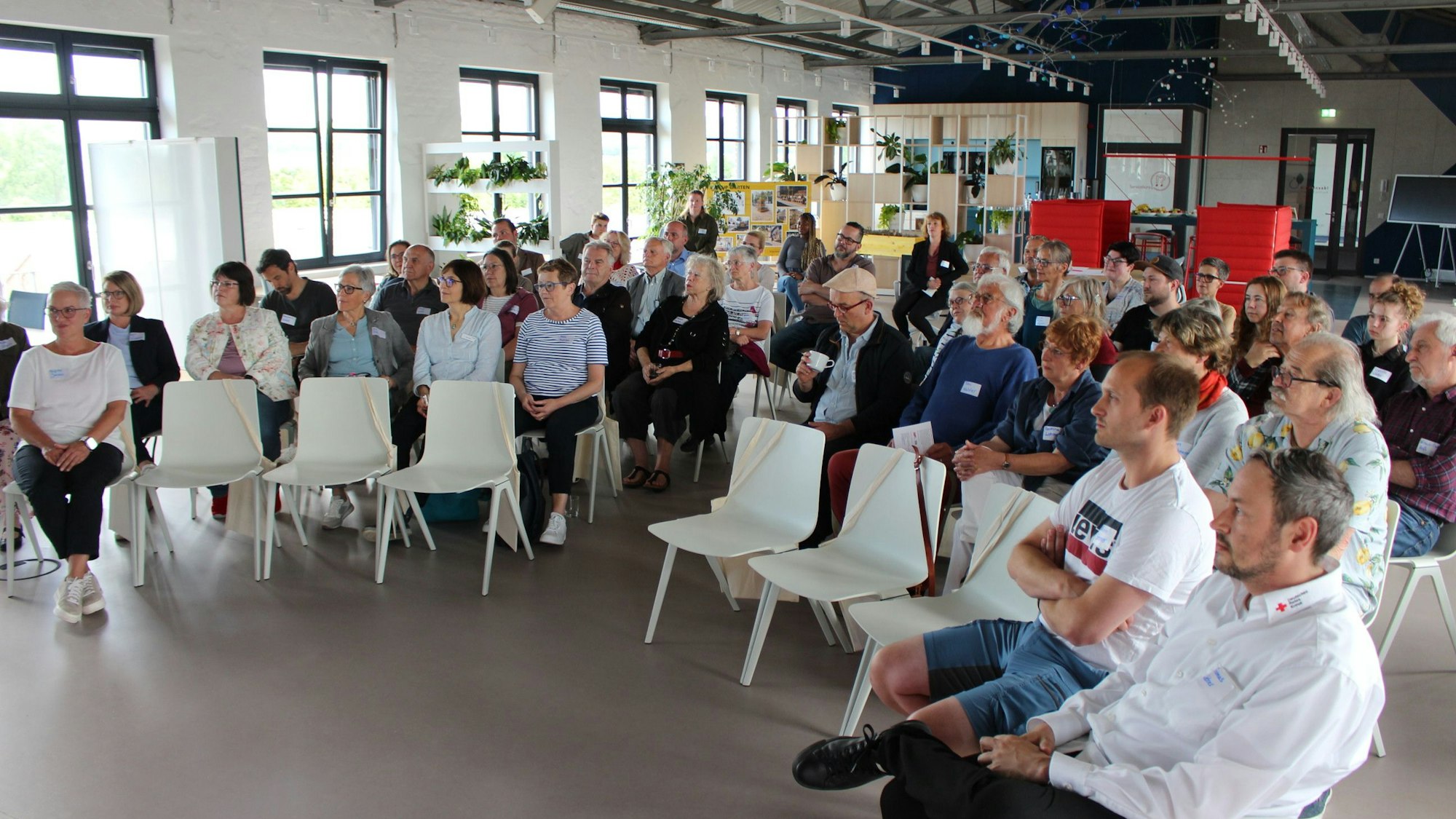 Die Teilnehmerinnen und Teilnehmer haben in den Stuhlreihen Platz genommen.
