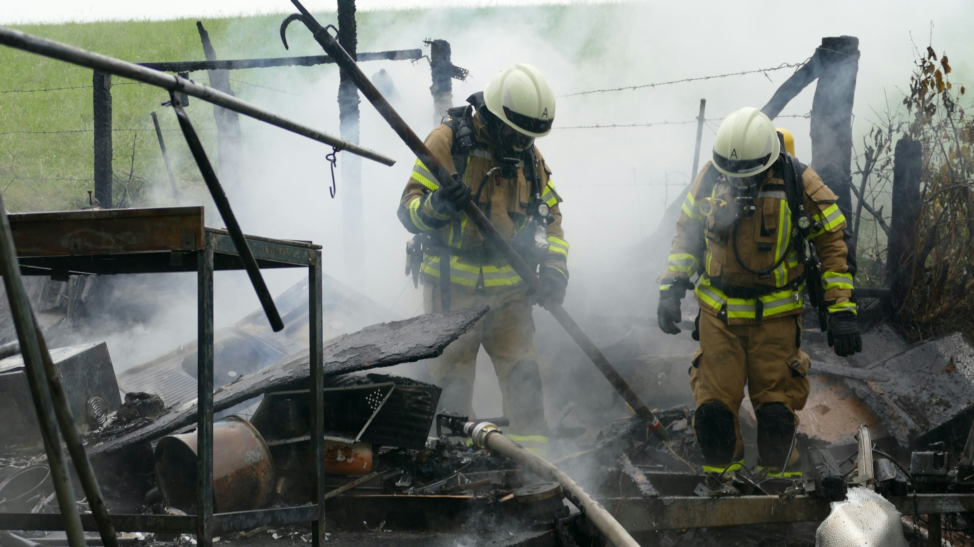 Zwei Feuerwehrleute stehen in Brandschutt.
