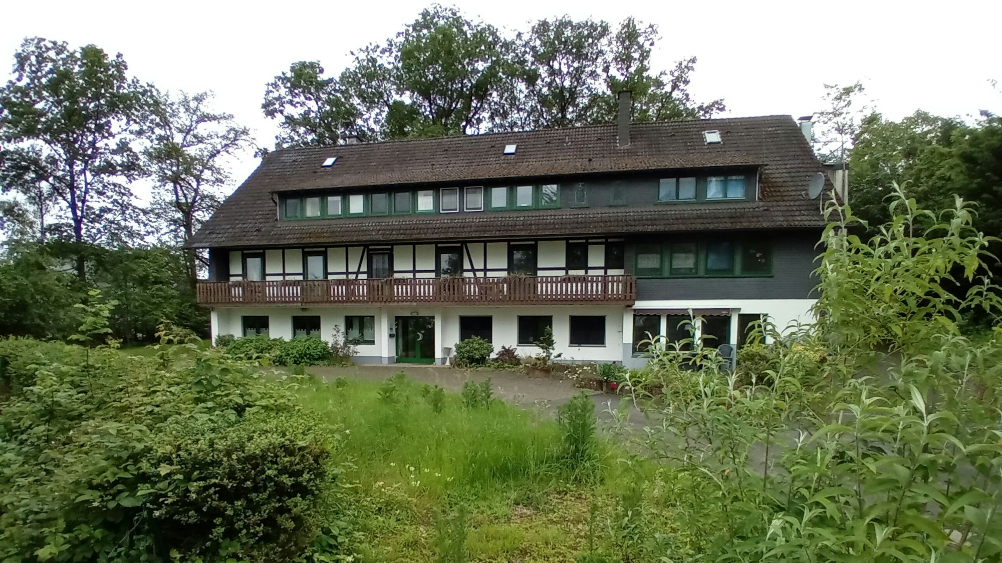 Ein dreigeschossiges Haus in einem verwilderten Garten.