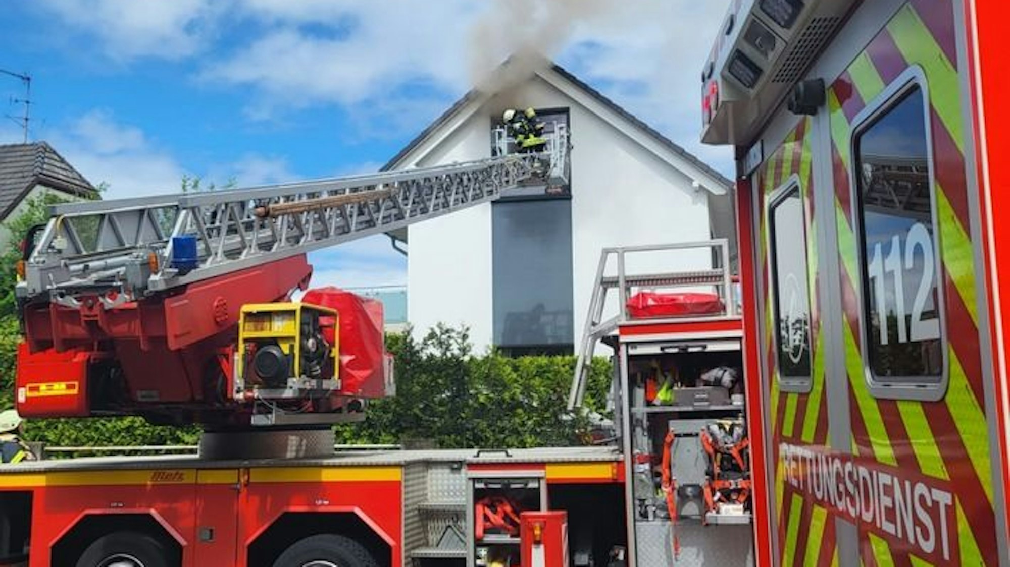 Es ist zu erkennen, wie Feuerwehrleute über eine Drehleiter in ein Zimmer einrücken.