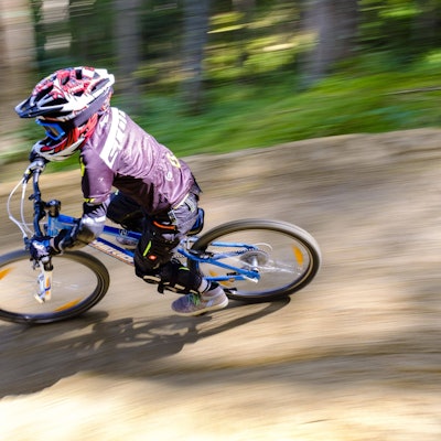 Ein Kind, 9 Jahre alt, fährt auf einem Mountainbike downhill, Es trägt Schutzausrüstung, aber die Geschwindigkeit zeigt sich in der verschwommenen Umgebung.