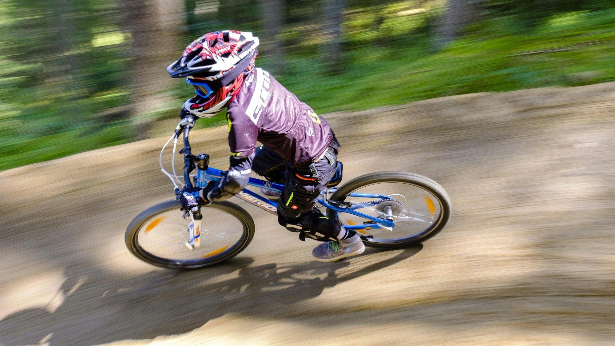 Ein Kind, 9 Jahre alt, fährt auf einem Mountainbike downhill, Es trägt Schutzausrüstung, aber die Geschwindigkeit zeigt sich in der verschwommenen Umgebung.