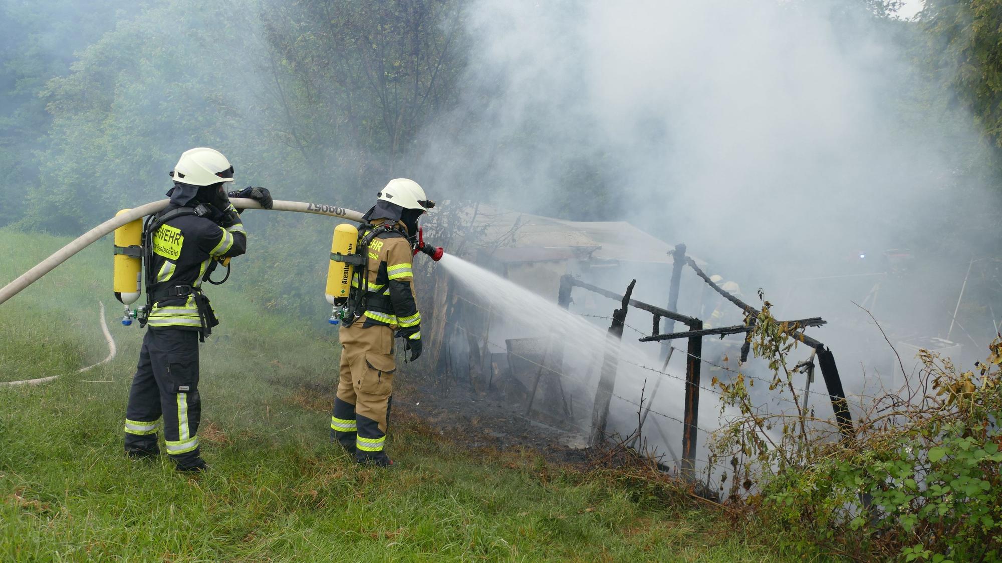 Feuerwehrleute löschen unter Atemschutz den niedergebrannten Wohnwagen.