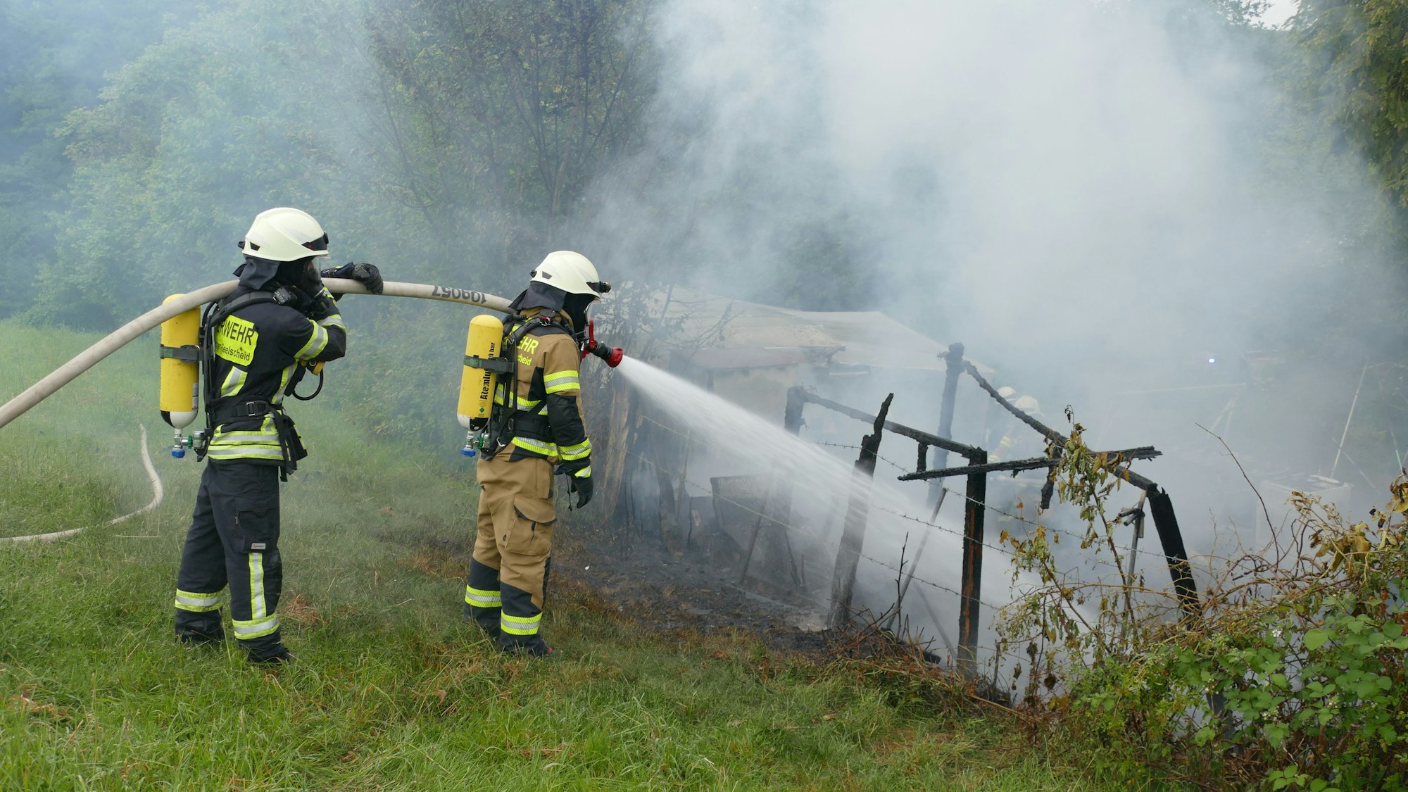 Feuerwehrleute löschen unter Atemschutz den niedergebrannten Wohnwagen.