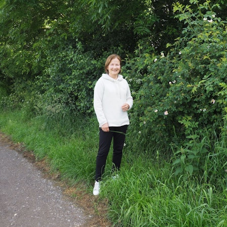 Petra Augel steht vor einem blühenden Rosenstrauch.