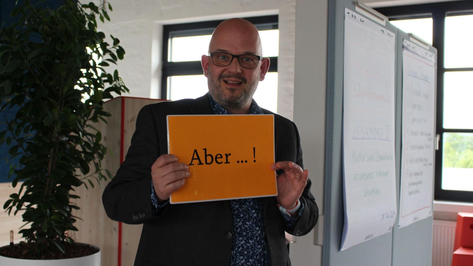 Tim Becker zeigt ein Schild mit der Aufschrift „Aber“.
