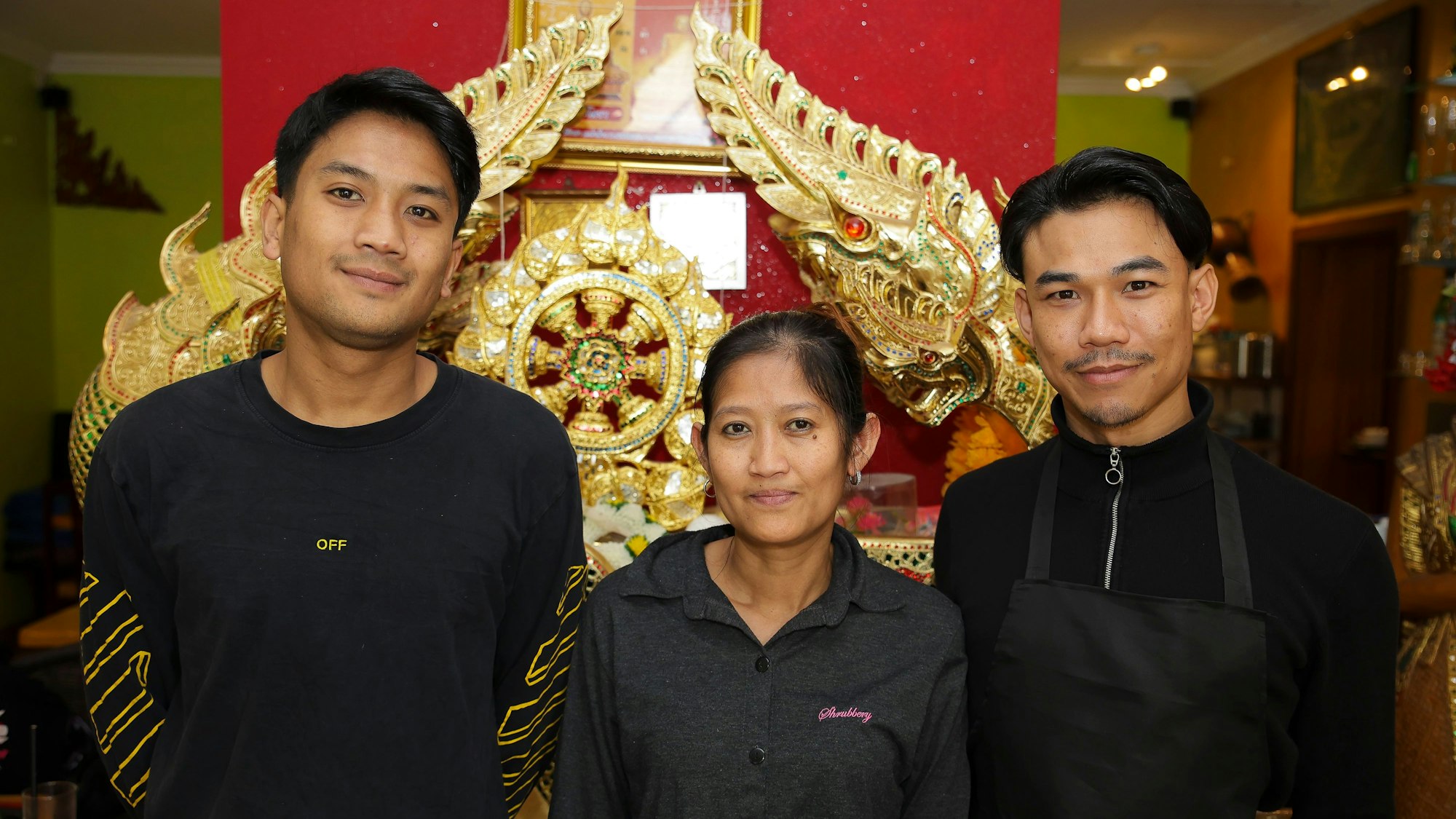 Drei Personen sind im Restaurant im Porträt zu sehen:Thaua Nakornchai (Sohn der Betreiber-Familie und Manager), Prangthiep Samuwanitt, die Geschäftsführerin und Kittisak Charattree, der stellvertretende Manager des Thai Restaurants Chok Dee. Im Hintergrund ist eine golden-ornamentale Skulptur zu sehen.