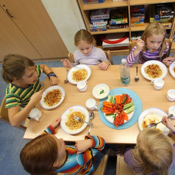 Kinder sitzen zum gemeinsamen Essen an einem Tisch,