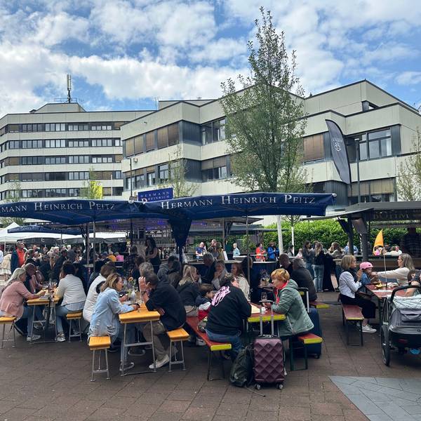Menschen sitzen beim Weinfest in Siegburg auf Bierbänken.